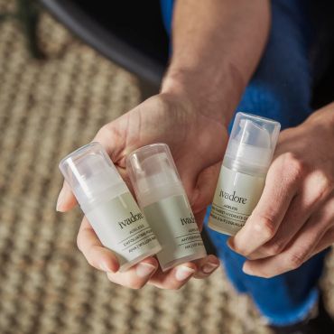 Hands holding three Ivadoce skincare product bottles with pump dispensers.
