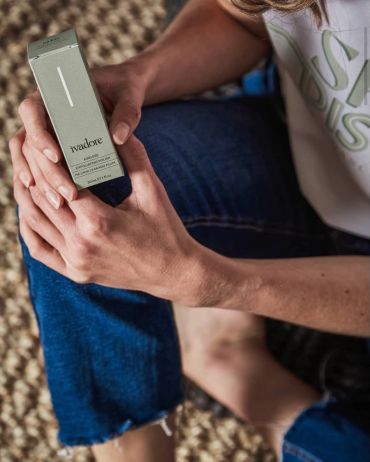 Person holding an Ivadore skincare product box while sitting cross-legged.