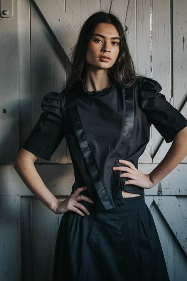 Woman in a stylish black outfit with hands on hips.
