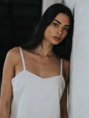 Woman in white dress leaning against a wall.