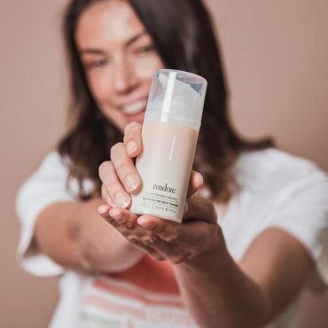 Woman holding a skincare product bottle with a smile.