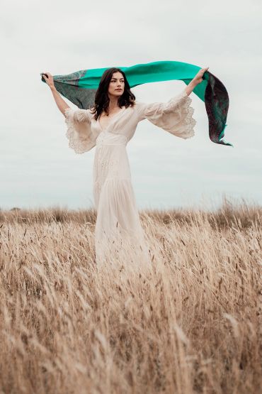 Woman in white dress holding a green scarf in a field.