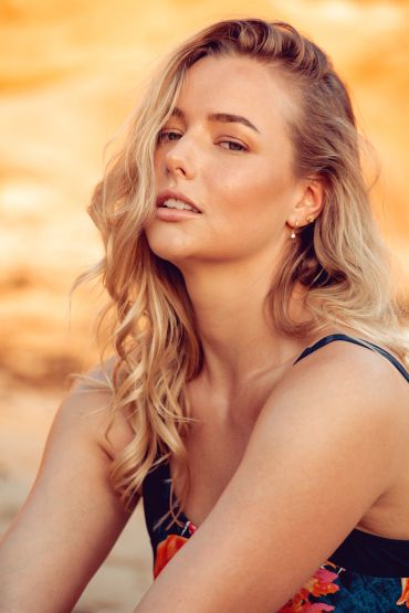 Blonde woman with wavy hair posing outdoors in warm light.