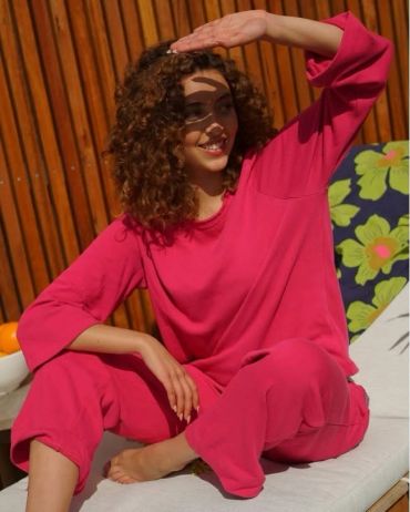 Woman in bright pink outfit shading her eyes, smiling.