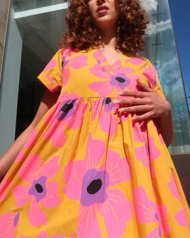 Woman in a vibrant yellow dress with pink and purple flowers.