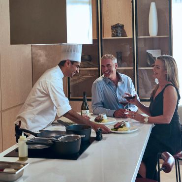 Chef serving food to a happy couple at a counter.