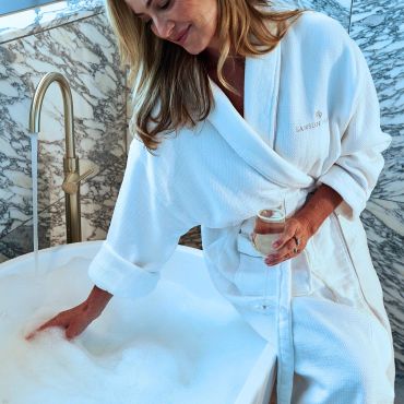 Woman in a white robe enjoying a bubble bath with a glass of wine.