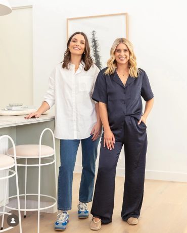 Two women standing in a bright room, smiling and casually dressed.