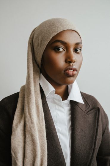 Confident woman wearing a beige headscarf and dark coat.