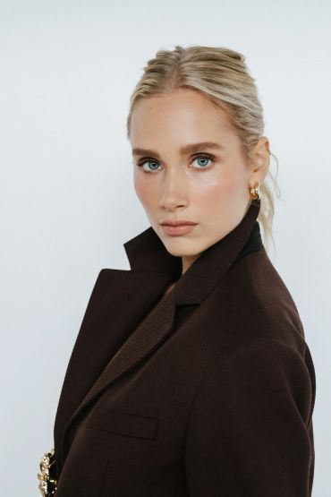 Elegant woman with blonde hair wearing a dark blazer and gold earrings.
