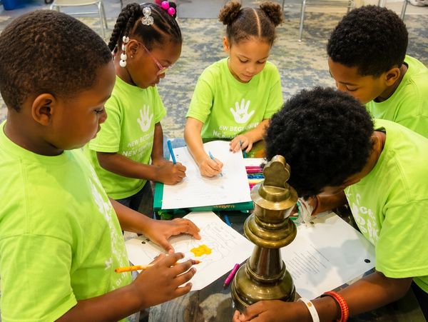 Kids in green shirts working on papers around a table.