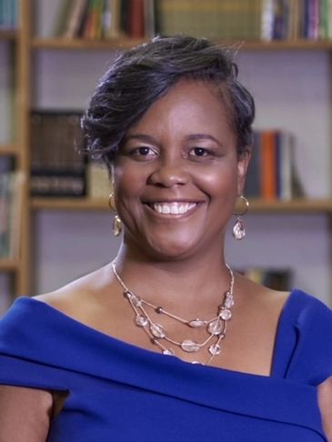 Smiling woman with short hair and earrings in front of a bookshelf.