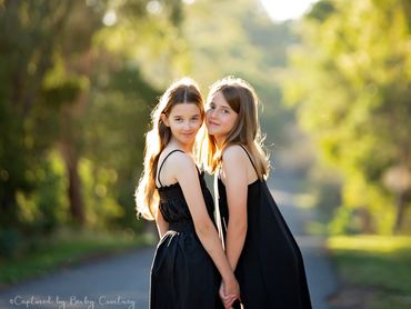 Two 11 year old girls holding hands with tree background and sun glistering, they are best friends a
