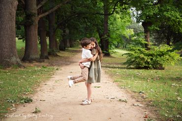 big sister is lifting her little brother off the ground for a big cuddle in the park surrounded by t