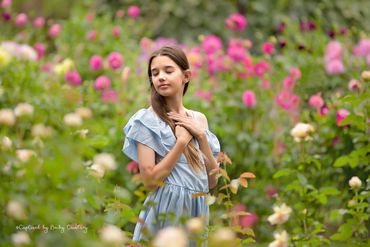Little girl standing in the middle of a flower field with her hands folded on her heart with a relax