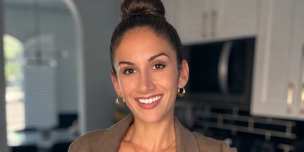 A smiling woman with a brown blazer stands in a modern kitchen.