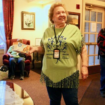 Elderly woman smiling in a green Alaska t-shirt indoors.