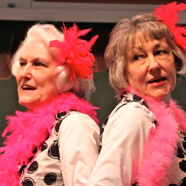 Two elderly women dressed in vibrant feather boas.