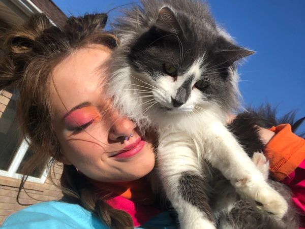 Woman with colorful makeup holding a fluffy gray and white cat.