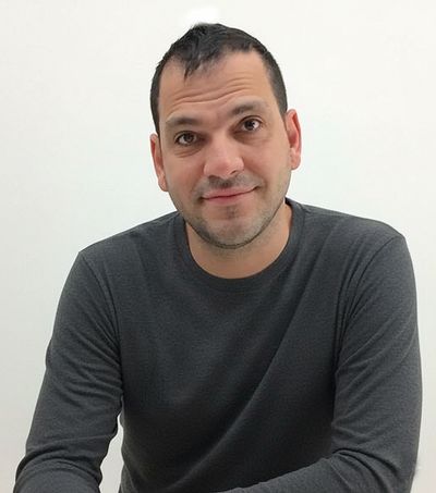 Man in dark gray long-sleeve shirt smiling against a plain white background.