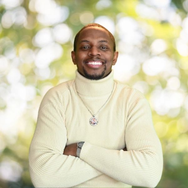 Smiling man in a cream turtleneck sweater with arms crossed.