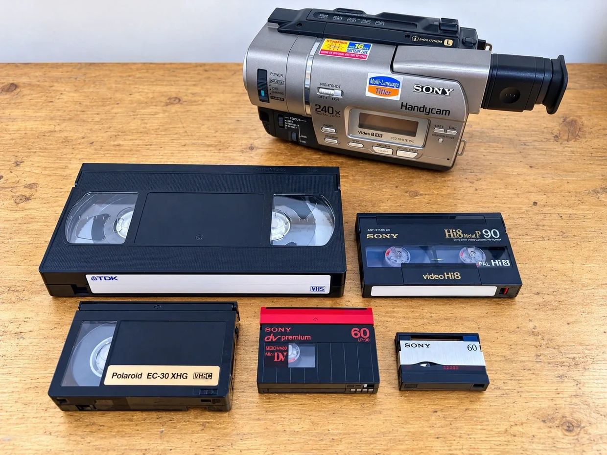 Various vintage video tapes and a Sony Handycam on a wooden table.