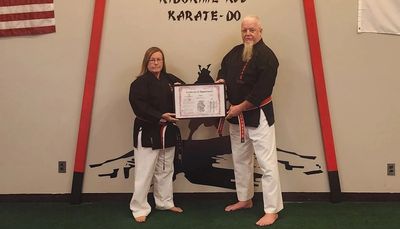 Two martial artists holding a certificate in a dojo with a karate logo.