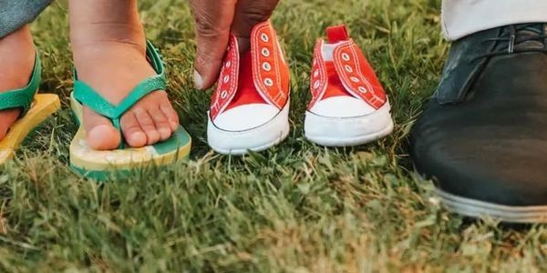 Line up of shoes, dad then child then empty baby shoes to represent waiting for a baby to adopt
