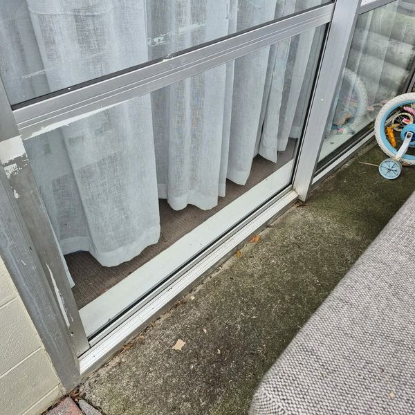 Sliding glass door with white curtains and a child's tricycle nearby.