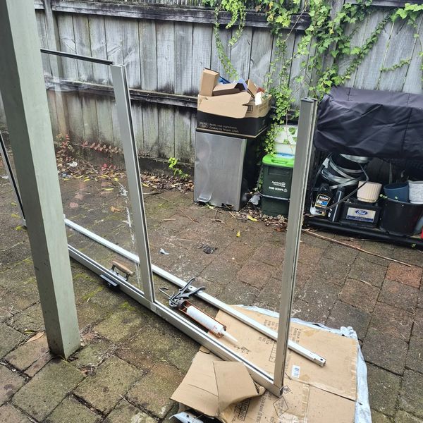 Disassembled glass door frame lying on cardboard outdoors.