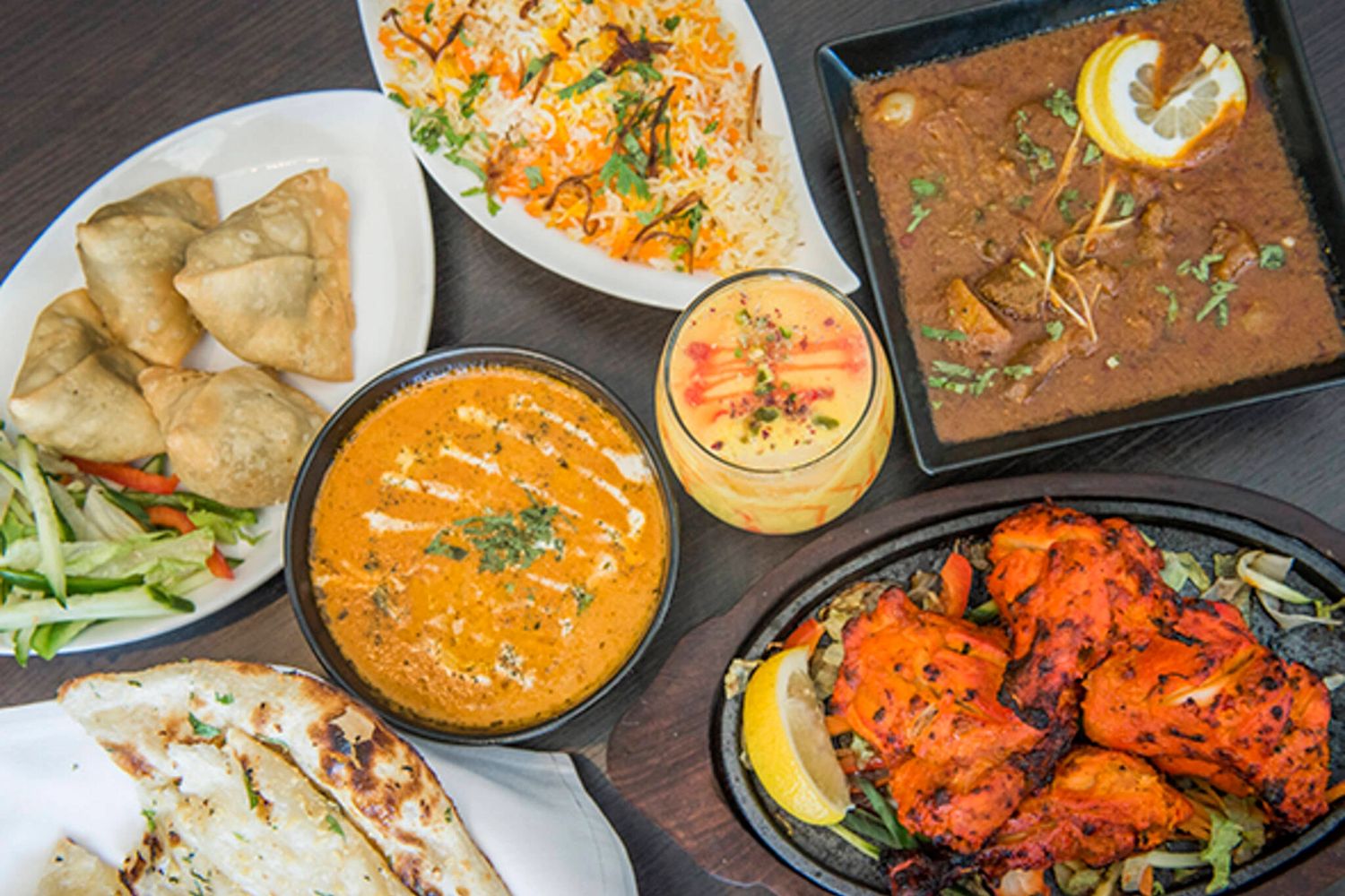 A spread of Indian dishes including samosas, naan, curry, rice, and tandoori chicken.