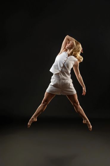 Woman in white jumps against dark background.