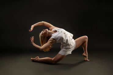 Woman performing a graceful dance pose in white outfit.