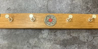 Wooden coat rack with five hooks and an emblem in the center.