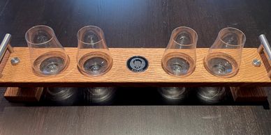 Wooden flight paddle with four empty glasses on a dark table.