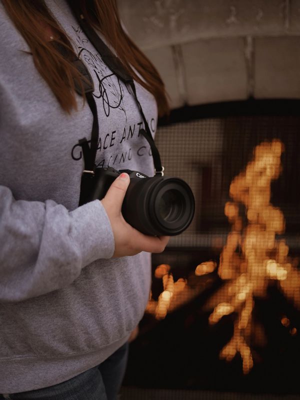 Person holding a Canon camera near a cozy fireplace.