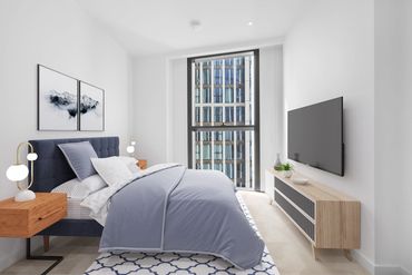 Modern bedroom with blue bedding, wooden nightstands, and a large window overlooking a building.
