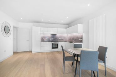 Modern kitchen with white cabinets, light wood flooring, and a small dining table with gray chairs.