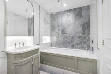 Modern bathroom with gray and white marble tiles and a sleek bathtub.