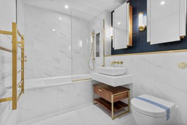 Modern bathroom with white marble tiles and gold accents.