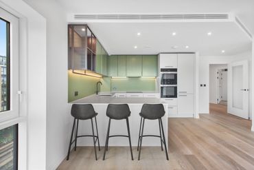 Modern kitchen with green cabinets, white island, and black stools.