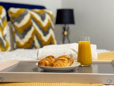 Breakfast tray with croissants and orange juice on a bed with patterned pillows.