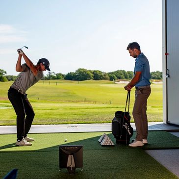 A golfer at a club fitting being coached while at the top of his backswing. 