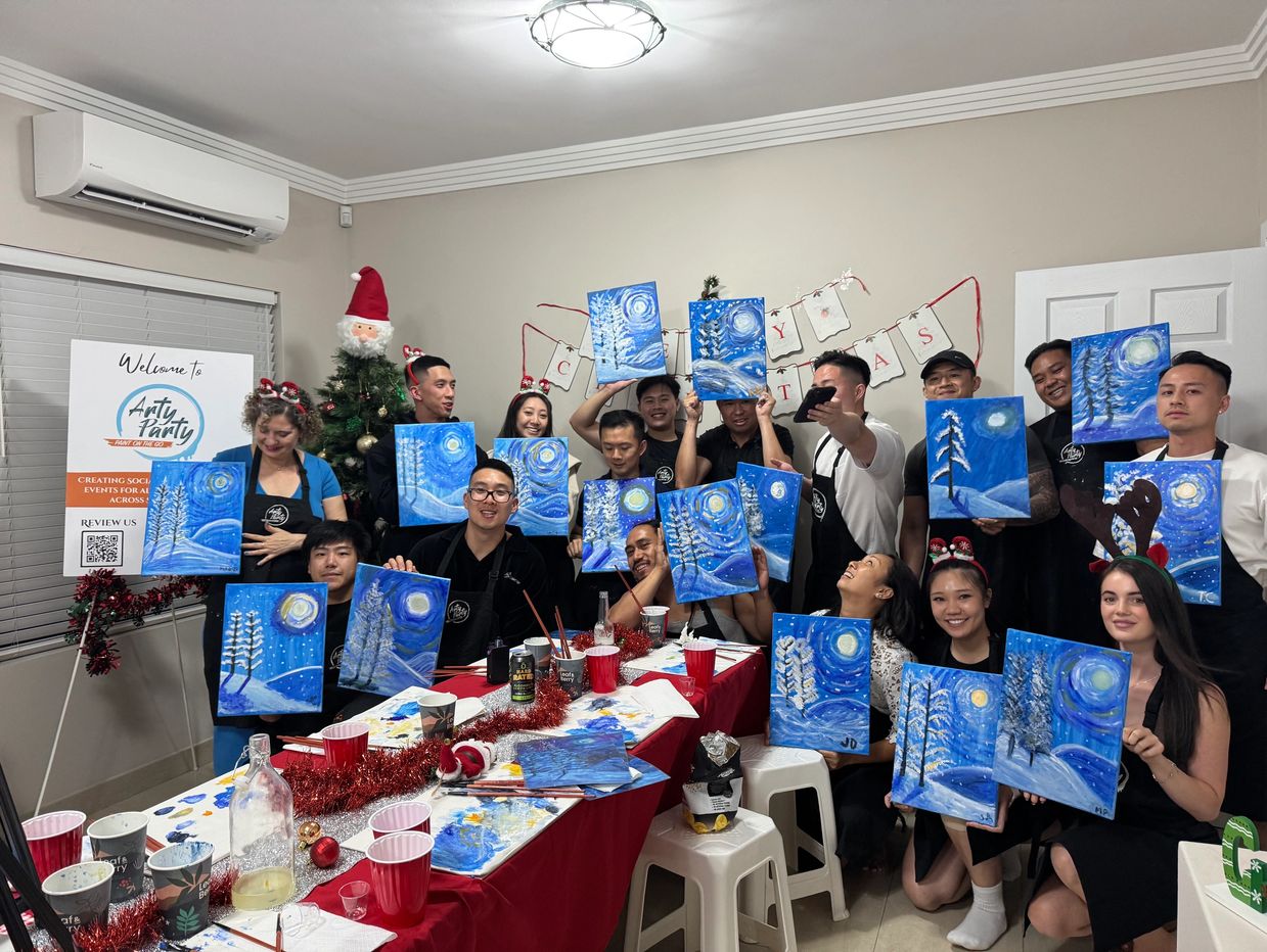 Group celebrating Christmas with winter-themed paintings at an art party.