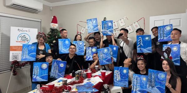 Group celebrating Christmas with winter-themed paintings at an art party.
