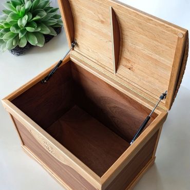 Open wooden chest with natural finish and a green plant beside it.