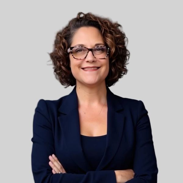 Confident woman with curly hair and glasses smiling, dressed in a navy blazer.
