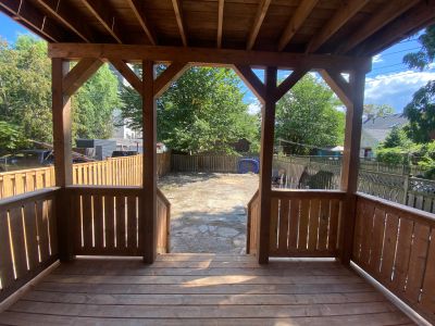 View from a wooden porch to a backyard with trees and a stone patio.