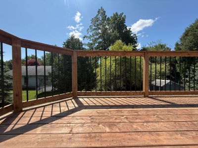 Sunlit wooden deck with black railing on a clear day.