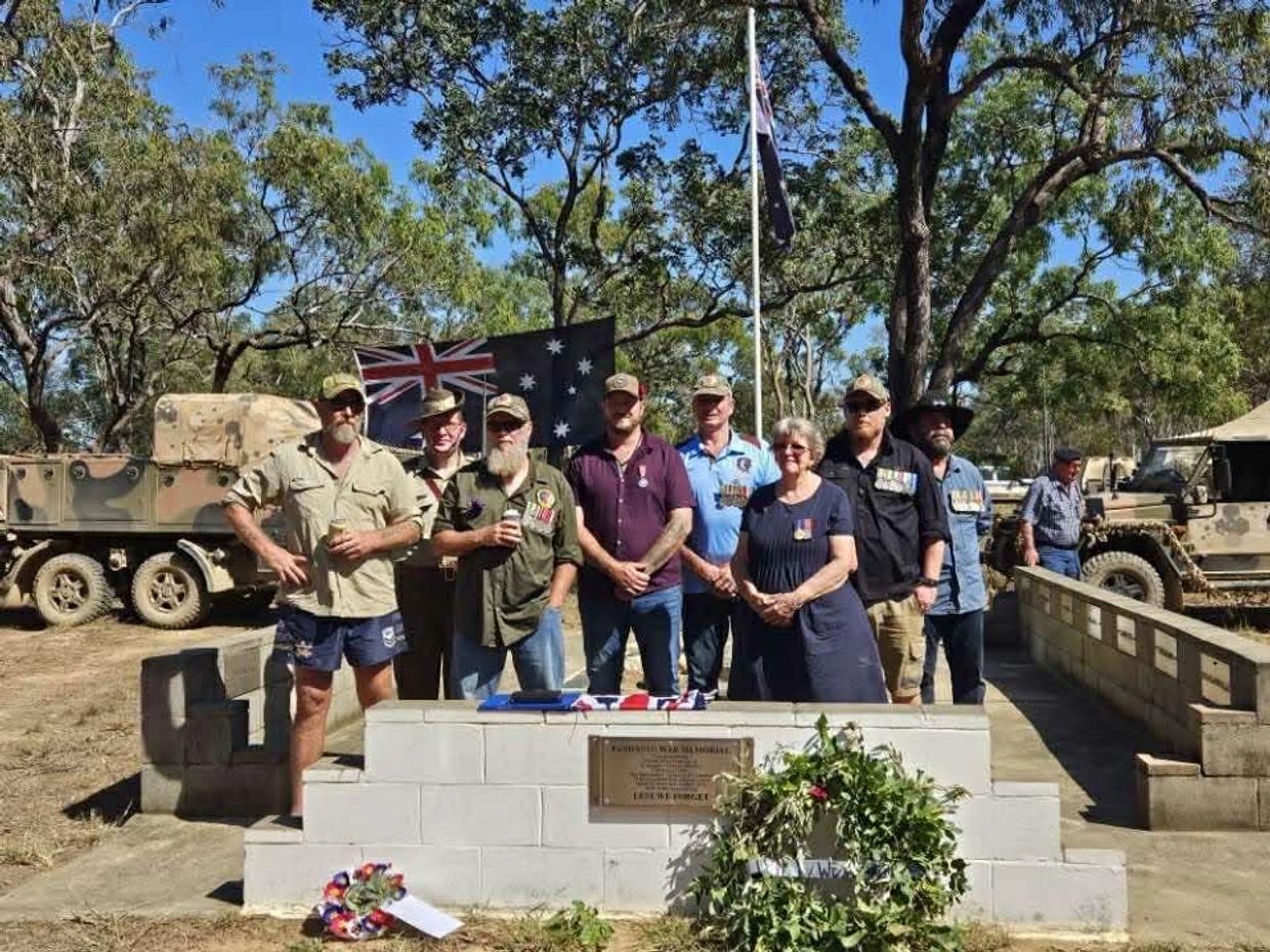 Group of veterans and civilians at a war memorial with Australian flags and military vehicles.